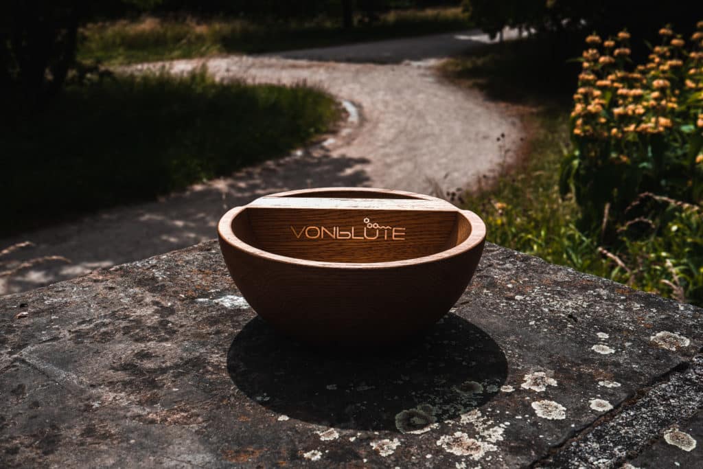 The Bowl Mischeschale aus Eichenholz mit Edelstahl-Logo, inszeniert im sommerlichen Naturambiente