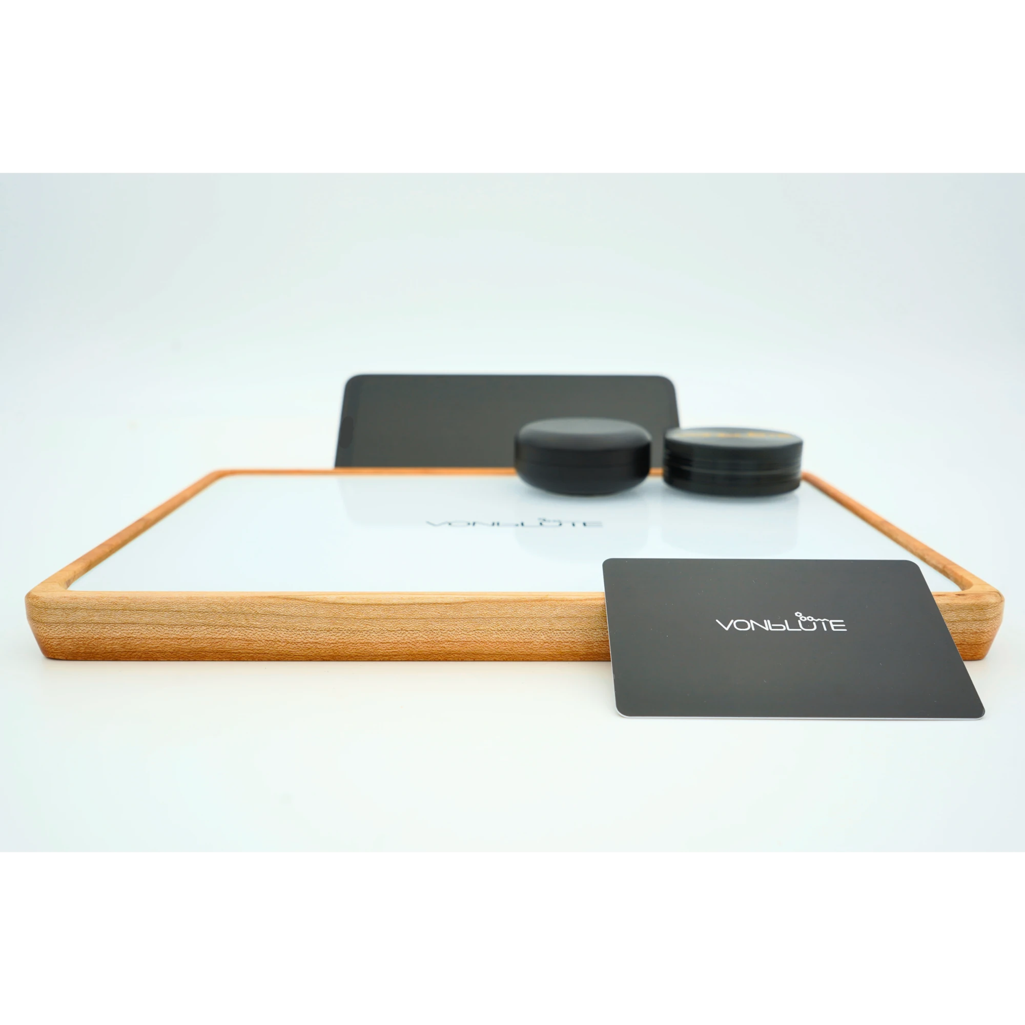 Rolling Tray Float Red Tone Weiss Edition Black in Frontaler Ansicht mit adaptiertem Handy, schwarzem Zubehör, Grinder und Dose, Mischkarte lehnt Frontal am Nussholzrahmen.